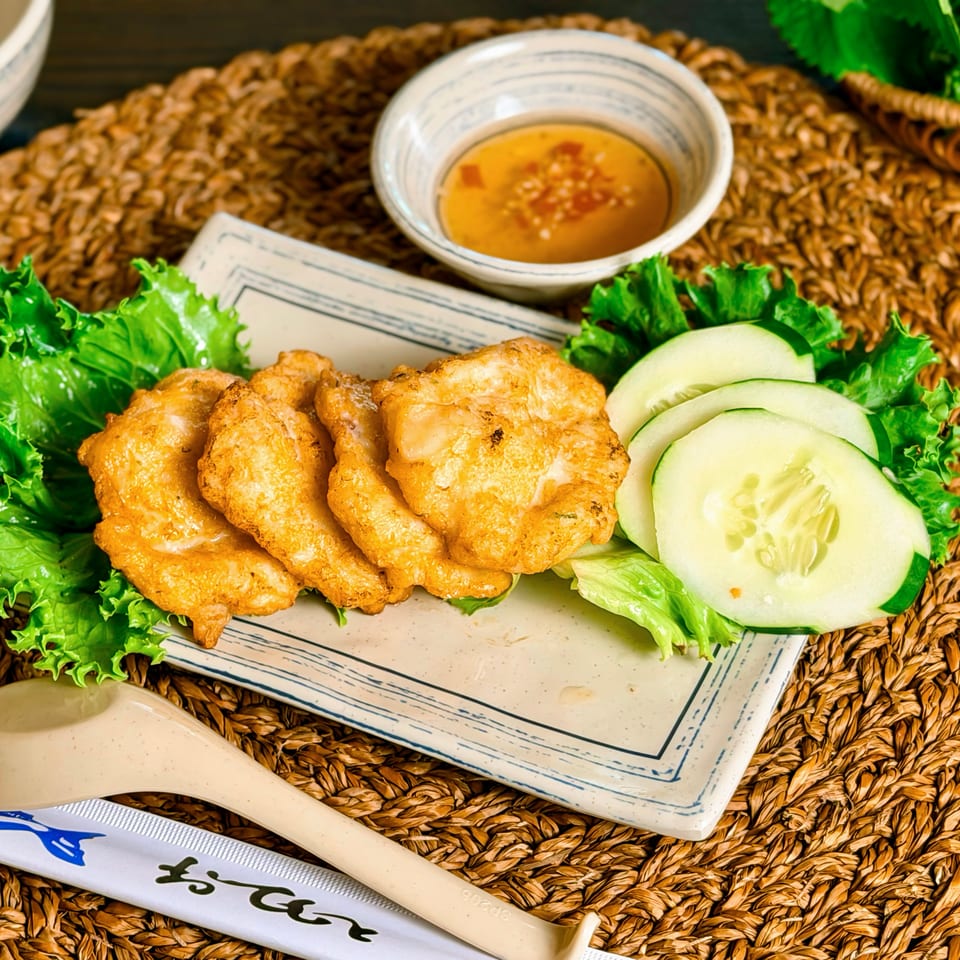 Crispy fried chicken pieces with lettuce and cucumber slices on a rectangular plate, served with dipping sauce.