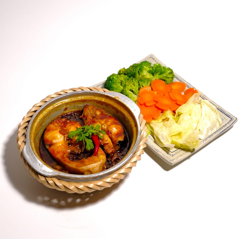 Glazed chicken stew in a clay pot with chili and herbs, served alongside broccoli, sliced carrots, and cabbage.