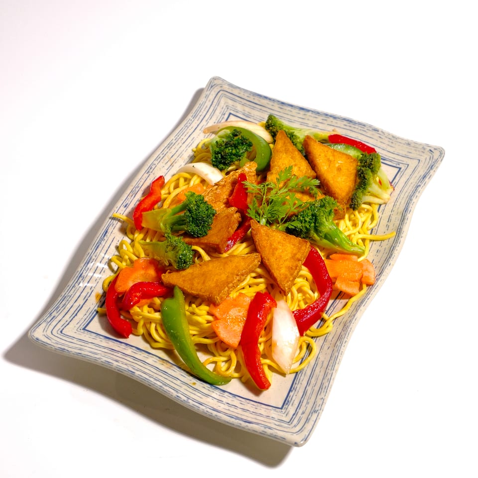 Plate of yellow noodles topped with crispy triangular pieces, broccoli, bell peppers, carrots, and cabbage.